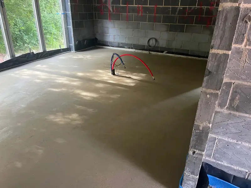 Extension floor screed beside a glazed wall with pipework left exposed for connection