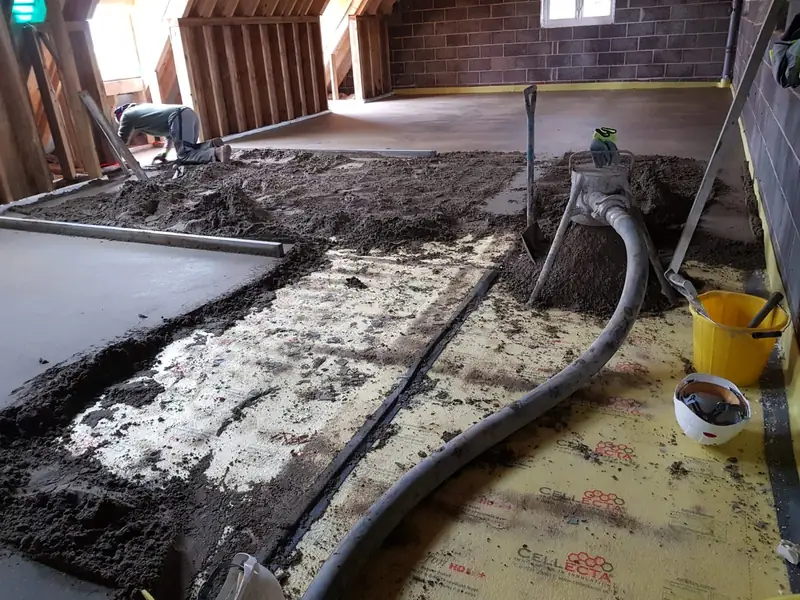 Screed being pumped by hose over underfloor heating pipework, with the first section already levelled