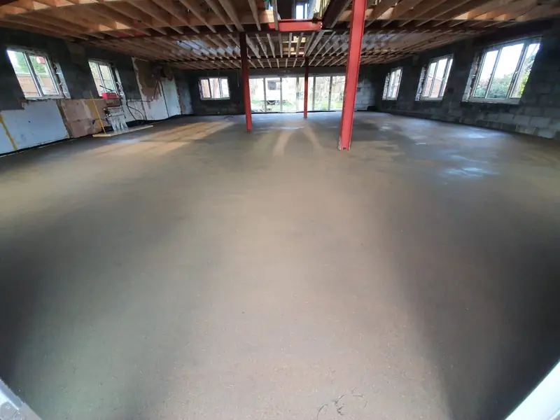 Freshly laid sand and cement screed across a large open-plan new-build ground floor with exposed roof joists