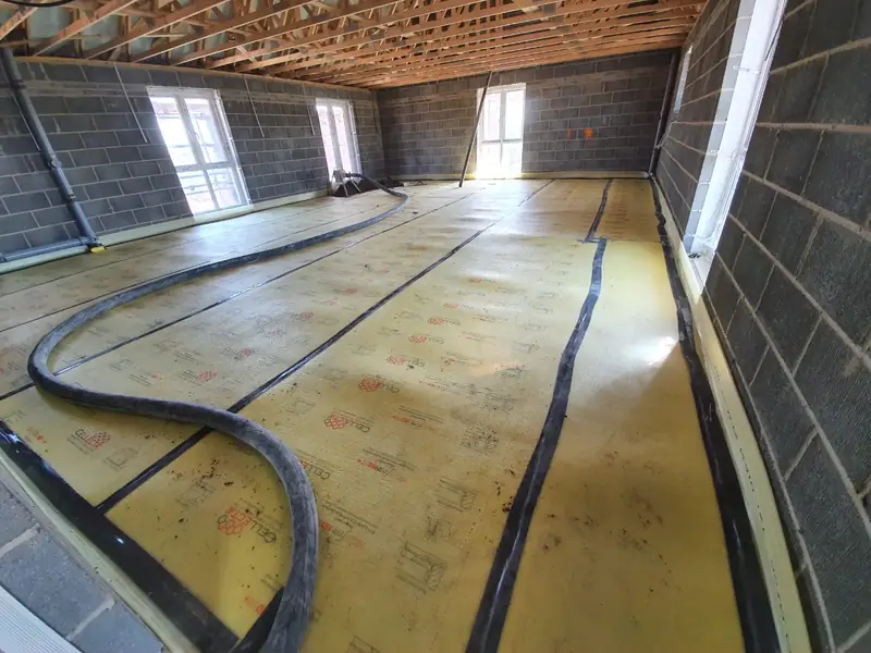 Screed delivery hose run across a prepared floor with insulation and heating zones marked out