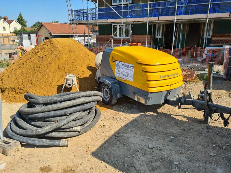 Yellow screed pump with delivery hoses beside a sand pile on a residential building site